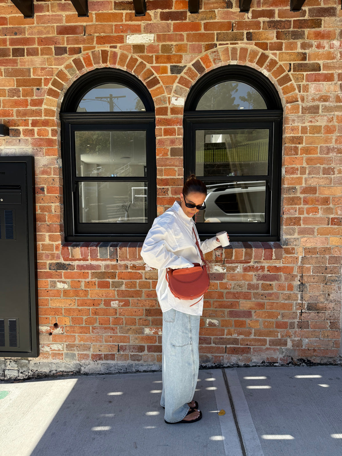 Person standing against a brick wall with a red handbag